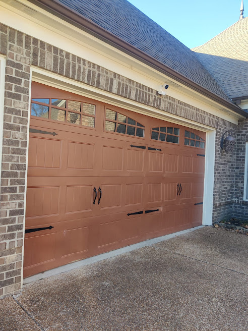 Finished red carriage-style garage door with glass panels and decorative hardware