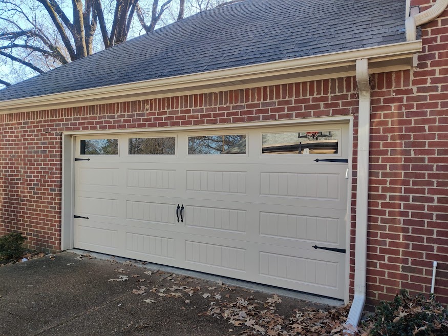 Finished white carriage-style garage door with rectangular windows on a brick home