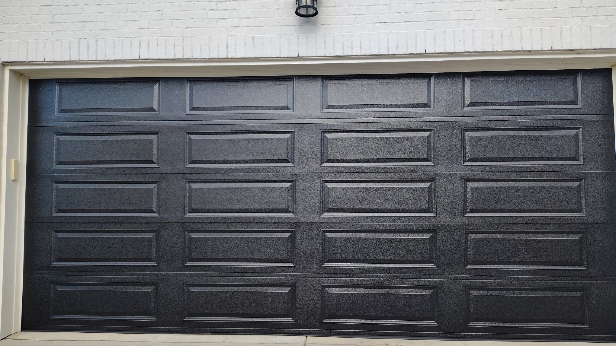Finished black raised-panel garage door installed on a white brick home in Greater Memphis