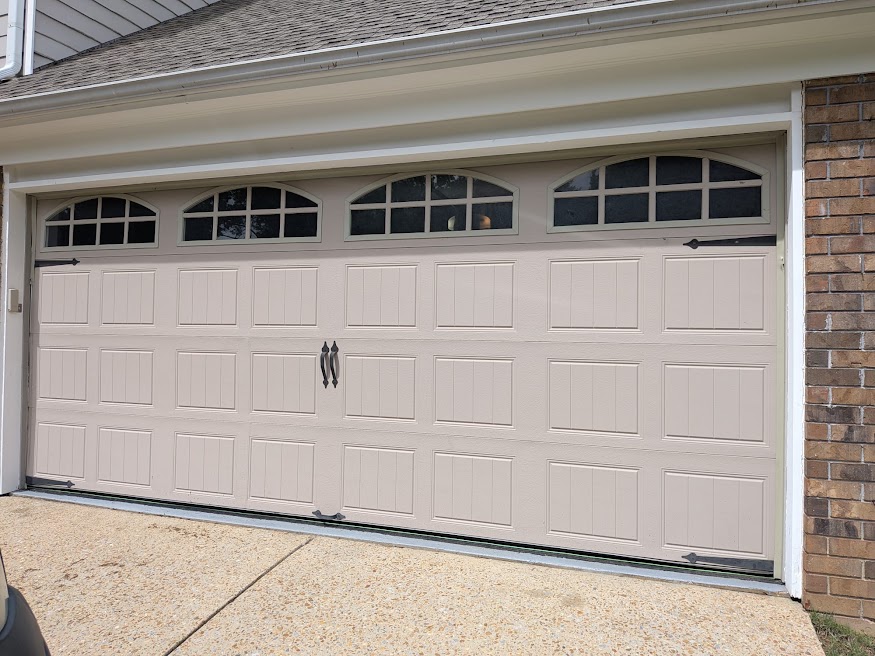 Finished cream carriage-style garage door with arched windows and decorative hardware